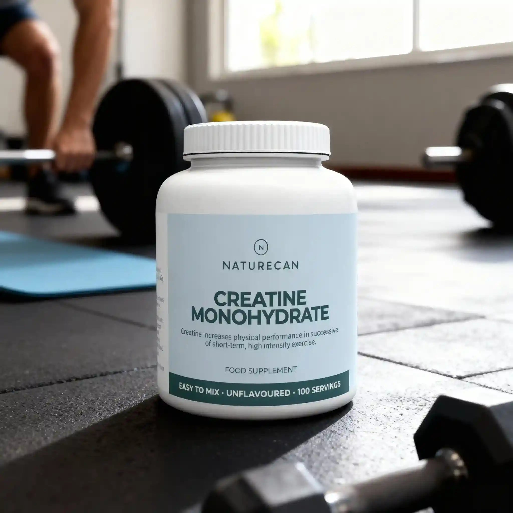 Naturecan Creatine Monohydrate supplement bottle on a gym floor with weights and exercise equipment in the background.