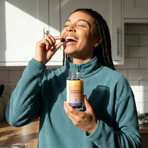 Woman in a kitchen holding a bottle of Shilajit Gummies and a gummy.